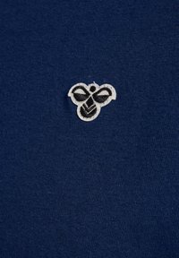 Mörkblå bomullsduk med en strukturerad, broderad svart och vit bi-logotyp placerad på vänster sida.