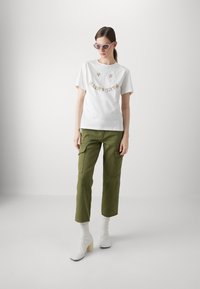 Witte katoen t-shirt met kleurrijke bloemenborduring, gecombineerd met olijfgroene cargobroeken en witte stretch enkellaarsjes met blokhakken.