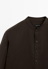 Dark brown linen shirt with a mandarin collar, featuring a button placket and a textured fabric. Label visible inside the collar.