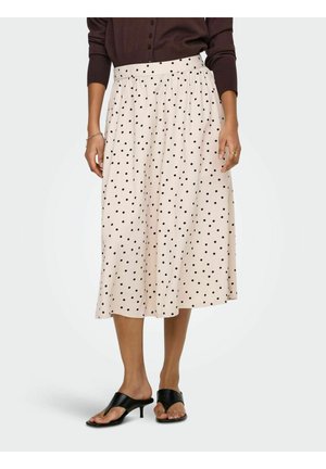 Femme portant une jupe midi beige à pois noirs, des sandales à talons noires, et un haut à manches longues marron foncé.