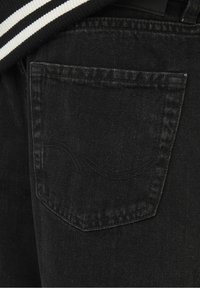 Tasca posteriore di jeans in denim nero con cuciture curve sottili, accanto a un tessuto a righe bianche e nere.