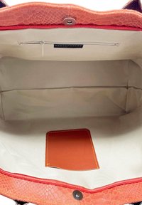 Pomarańczowe, fakturowane wnętrze torebki z jasną tkaniną podszewkową, małą brązową skórzaną kieszonką oraz komorą na zamek na górze.