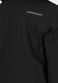 Veste noire au tissu lisse ; avec le logo blanc "SWEDEMOUNT" au dos. Design épuré avec un empiècement courbé et sans embellissements supplémentaires.