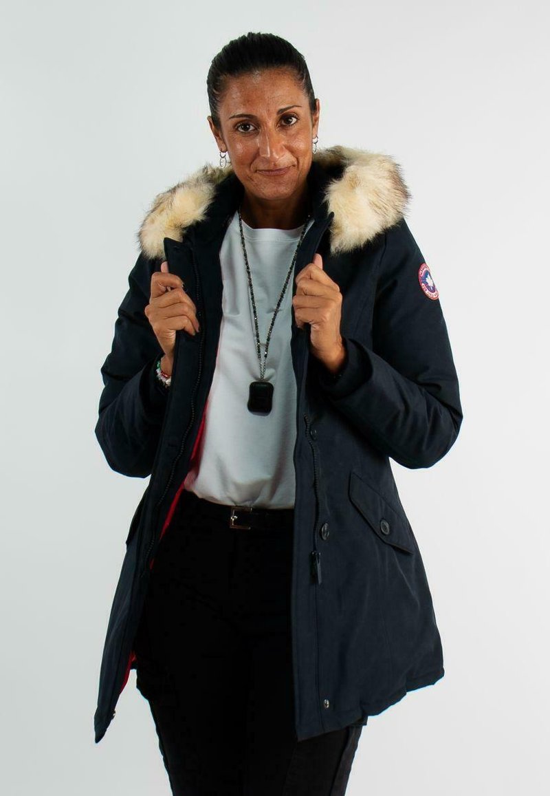 Parka bleu marine avec capuche en fausse fourrure, fermeture éclair sur le devant et poches latérales. L'intérieur est en tissu rouge, conçu pour les temps froids.
