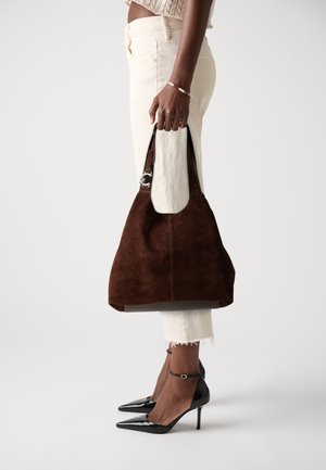 Brun ruskinds skuldertaske med en afslappet design, der har en rund top og en flad rem. Bæres med cremefarvede jeans og sorte hæle.
