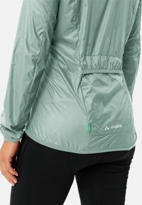 Lichtgewicht, mintgroene jas met een glanzende afwerking, elastische manchetten en een geraffineerd rugontwerp. Beschikt over een klein groen accentlabel en logo.
