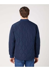 Granatowa pikowana kurtka z teksturowanym wzorem, z prążkowanym kołnierzem i mankietami. Posiada gładkie wykończenie i luźny krój.
