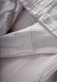 Hellgrauer Stoff mit einer weichen, strukturierten Oberfläche, der ein zerknittertes Aussehen und geschichtete Falten aufweist. Hergestellt aus einem atmungsaktiven Material.