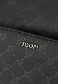 Musta kangaskotelo, jossa on teksturoitu kuvio, joka esittää pyöreitä muotoja. Hopeinen "JOOP!" -logo on näkyvästi esillä. Silkkinen pinta.