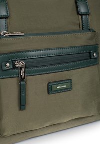 Olijfgroene nylon tas met een gladde textuur, voorzien van een donkergroene leren ritszak, zilverkleurige hardware en een rechthoekig merklabel.