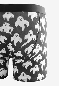 Schwarze Boxershorts mit weißen Gespenstermustern, ausgestattet mit einem schwarzen Bund und glatter Textur. Nähte sind entlang der Säume deutlich sichtbar.