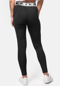Black leggings with a high waistband featuring white logo accents. Made from stretchy fabric, they offer a fitted design and smooth texture.
