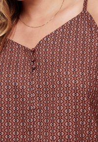 Bruine tanktop met een v-hals, voorzien van een knoopsluiting en ingewikkelde geometrische ontwerpen in lichte en donkere tinten.