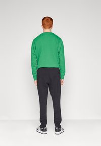 Camisa de mangas longas verde, calças de jogging pretas e ténis em preto e branco. Design simples, material de algodão, com punhos e cintura canelados.