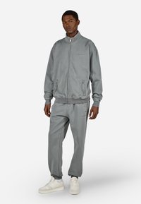 Pilkas užtrauktukas džemperis ir atitinkamos kelnės, pagamintos iš minkštos medžiagos. Yra raukiniai ant rankovių ir juosmens, šoninės kišenės ir subtilūs prekių ženklų akcentai.