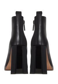 Botas de cuero negras hasta el tobillo con un tacón alto y cuadrado, que cuentan con cierre de cremallera y una textura suave en la parte superior.