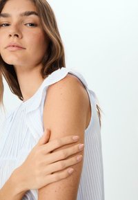 Plava i bijela prugasta majica bez rukava s naborima na ramenima; glatka tkanina koja se jasno prilagođava ramenu i ima laganu teksturu.