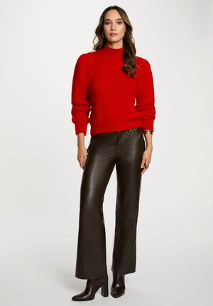Maglione rosso lavorato a maglia con collo alto e maniche a sbuffo abbinato a pantaloni in pelle nera a campana e stivali con tacco alto. Texture liscia.