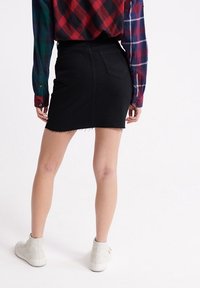 Svart denim minikjol med fransad nederkant, figurnära design och två bakfickor. Bärs med en rutig skjorta och vita hög-top sneakers.