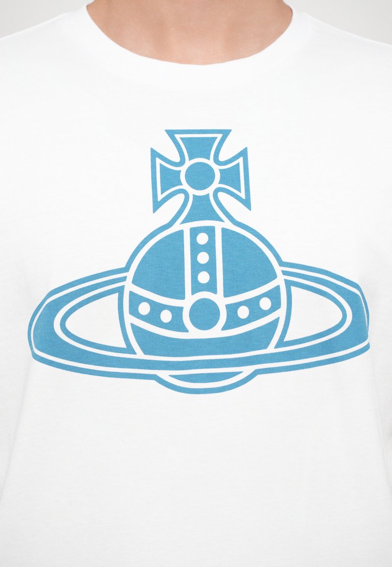 White t-shirt featuring a blue graphic design of a planet with rings and a cross symbol above it, with circular and linear details.