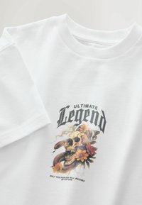 White cotton t-shirt with a crew neck, featuring a graphic print of a skull and flowers, with black text reading "ULTIMATE Legend."