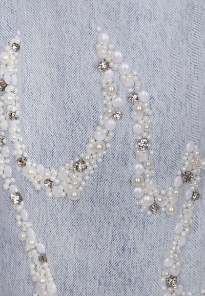 Tessuto in denim con un lavaggio azzurro chiaro, decorato con perline bianche e trasparenti disposte in motivi a onda, creando un contrasto testurizzato.