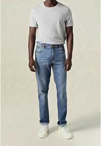 Hellblaue Jeans aus Denim mit geradem Schnitt, dezenten Verwaschungen und gesteppten Akzenten, kombiniert mit einem eng anliegenden grauen T-Shirt und weißen Sneakern.