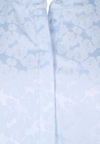 Himmelbluse aus leichtem Stoff mit einem strukturierten Blumenmuster, ausgestattet mit einer Knopfleiste. Der Stoff wirkt glatt, mit dezentem Glanz und weichem Fall.