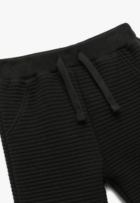 Sort ribbede sweatpants med elastisk talje, justerbar snor og sidelommer. Funktioner tekstureret stof og en tætsiddende pasform.