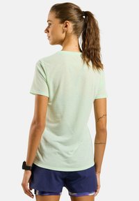 T-shirt de sport à manches courtes vert clair avec un motif texturé, coupe ajustée et col rond, associé à un short bleu marine.