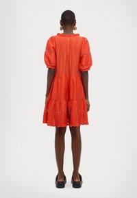 Czerwona sukienka z falbanami i bufkami, z falistym dekoltem i prążkowaną teksturą. W połączeniu z czarnymi butami na platformie.