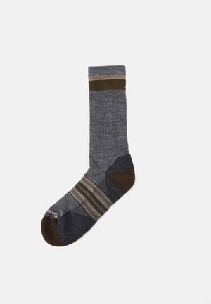 Grijze sok met ribbelpatroon, bruine en olijfgroene strepen, verstevigde teen en hiel, en contrasterende donkerblauwe accenten.