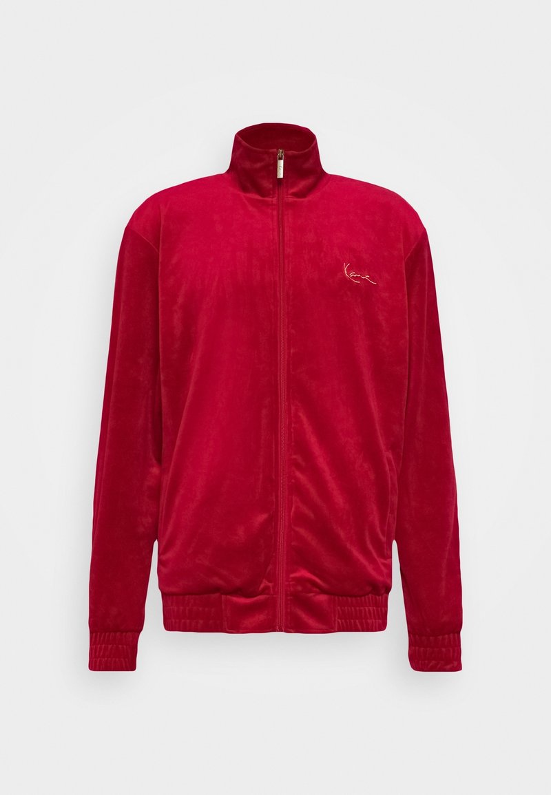 Veste zippée en velours rouge avec un col montant, des poignets et une taille élastiques. Présente un logo brodé discret sur la poitrine. Texture lisse.