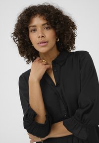 Czarna koszula z guzikami z kołnierzykiem, bufiastymi rękawami i marszczonymi mankietami; gładki materiał o eleganckim wykończeniu.