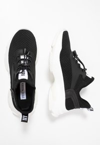 Baskets de sport en mesh noir avec une tige texturée, semelle blanche et lacets réglables. Comprend un logo et une languette de tirage à l'arrière.