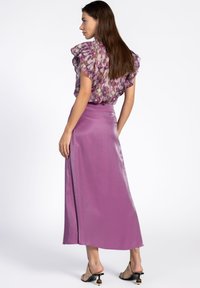 Paarse satijnen maxi rok met een gladde textuur, gecombineerd met een meerkleurige bloemen top met ruffles. Stiletto sandalen met een decoratieve hak.