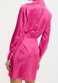 Abito in satin rosa con maniche lunghe, colletto e vita elastica. L'orlo è leggermente curvo, mostrando una texture liscia e lucida.