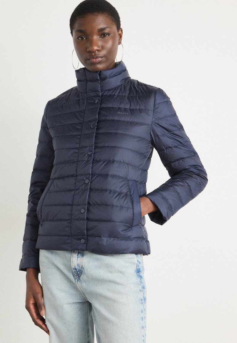 Giacca trapuntata blu navy con design a righe orizzontali, colletto alto, chiusura con bottoni e tasche laterali. Il tessuto appare lucido e morbido.