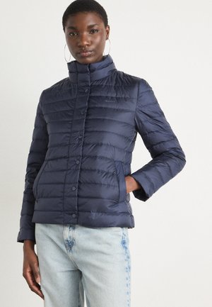 Veste à bomber marine avec un design matelassé horizontal, col montant, fermeture à boutons et poches latérales. Le tissu semble brillant et lisse.