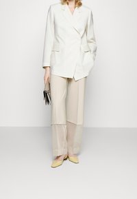 Dopasowana biała marynarka, jasnobeżowe spodnie o szerokich nogawkach i żółte buty na słupku. Charakteryzuje się czystymi liniami i gładką teksturą.