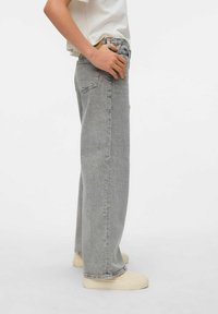 Jeans de pierna ancha en gris claro con una cintura alta, que cuentan con un diseño clásico de cinco bolsillos. La tela tiene una textura ligeramente desgastada.