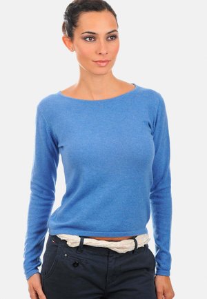 Pull bleu à manches longues en matière douce avec un col rond. Associé avec un pantalon foncé et une ceinture à motifs de couleur claire.