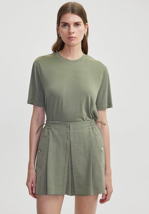 T-shirt vert olive avec une coupe décontractée, associé à un short taille haute avec des plis, des poches latérales et des détails de cordon.