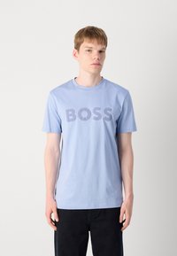T-shirt bleu clair en coton, arborant un grand logo « BOSS » bleu foncé sur la poitrine. Manches courtes et encolure ronde.