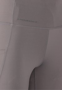 Grå atletiske leggings med en glat tekstur, der har flade sømme og ordet "ENDURANCE" trykt på siden.