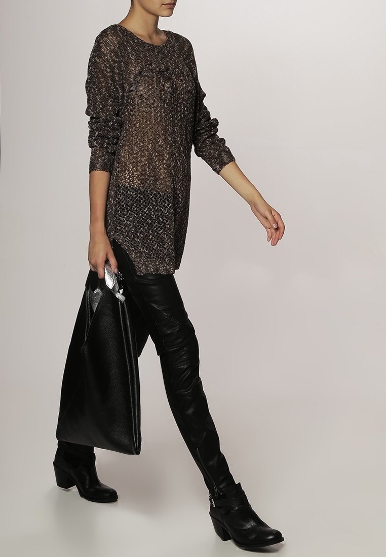 Übergroßer, transparenter Strickpullover mit strukturiertem Muster, Farbverlauf in Dunkelbraun und Schwarz, kombiniert mit eng anliegenden schwarzen Lederhosen und einer großen schwarzen Tasche.