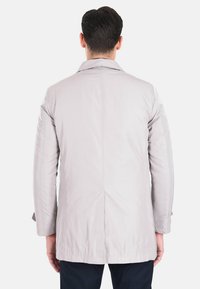 Cappotto grigio chiaro a maniche lunghe con taglio dritto, texture liscia e spacco posteriore. Presenta un colletto classico e cuciture minimaliste.