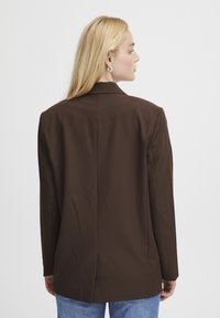 Blazer marron au design ajusté, avec une ouverture simple à l'arrière, des épaules structurées et des manches longues.
