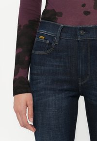 Donkerblauwe jeans met een klassiek ontwerp, stevige denim stof, gele merkaccenten en zichtbare stikseldetails.