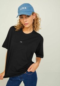 Black cotton T-shirt with a crew neckline and short sleeves, featuring small white logo. Paired with a light blue denim cap with white text.